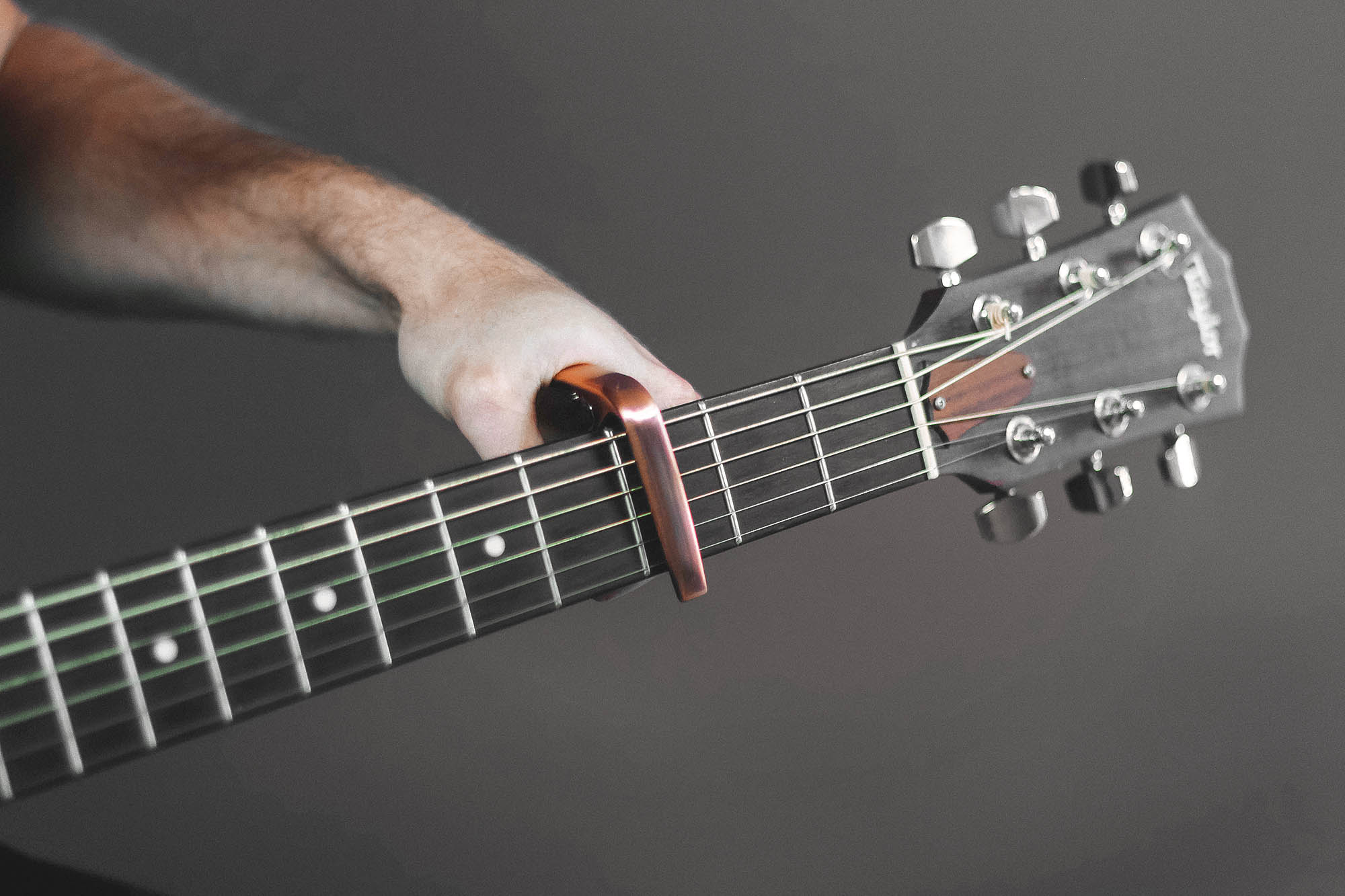 A hand placing a capo on the neck of an acoustic guitar